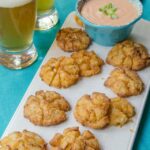 Bite-sized blooming onions on a tray with beer and dipping sauce in the background.