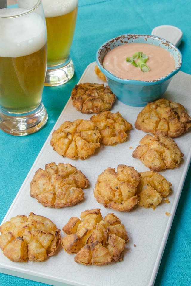 Bite-sized blooming onions on a tray with beer and dipping sauce in the background.