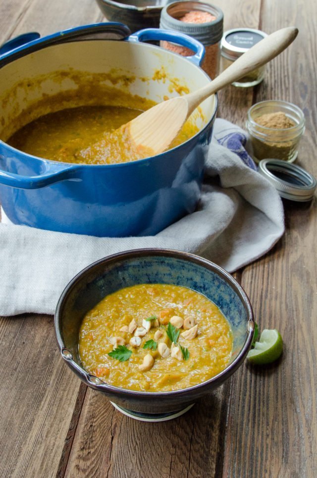 A bowl of mulligatawny on a wooden table with a blue Dutch oven in the background.
