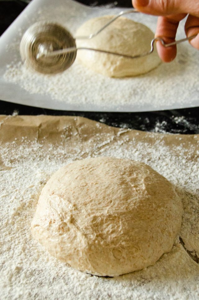 Whole wheat no knead bread being dusted with flour on floured parchment paper.