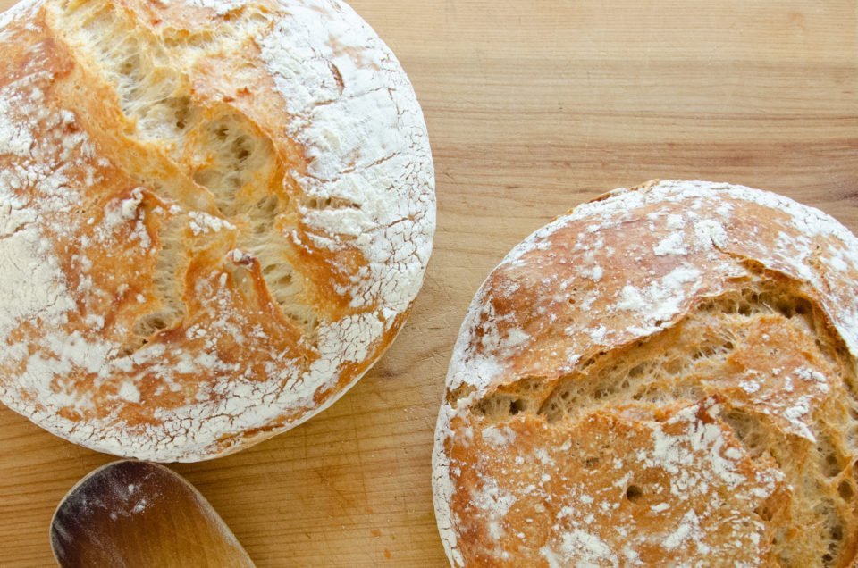 A loaf of white and whole wheat no knead bread on a wooden cutting board.