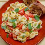 Creamy Corn and Tomato Orrecchiette in a red dish with crusty bread on the side.