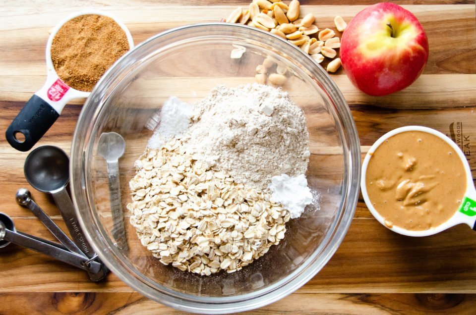 Ingredients for peanut butter breakfast bars in a glass bowl on a wooden cutting board.