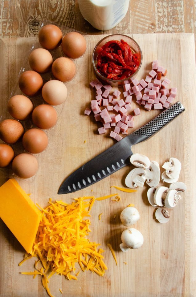 Ingredients for a frittata on a wooden cutting board with a knife.
