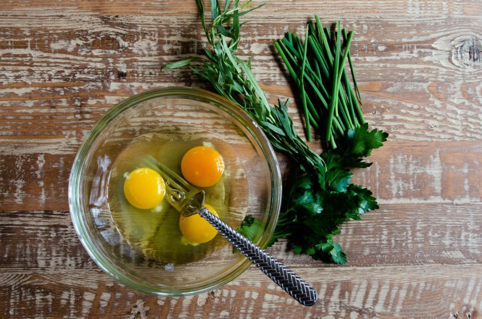 Three eggs, cracked in a bowl with fresh herbs on the table.