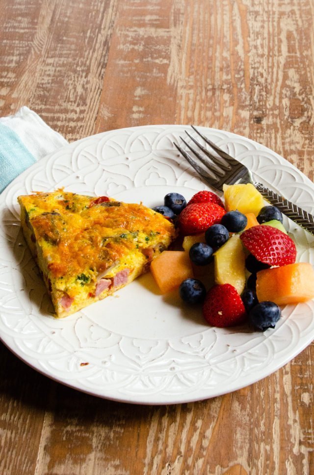 A wedge of frittata on a plate with some fruit.
