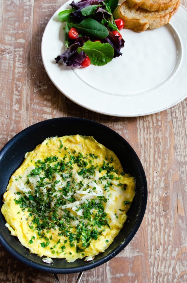 An omelet in a skillet before being folded onto a white plate.