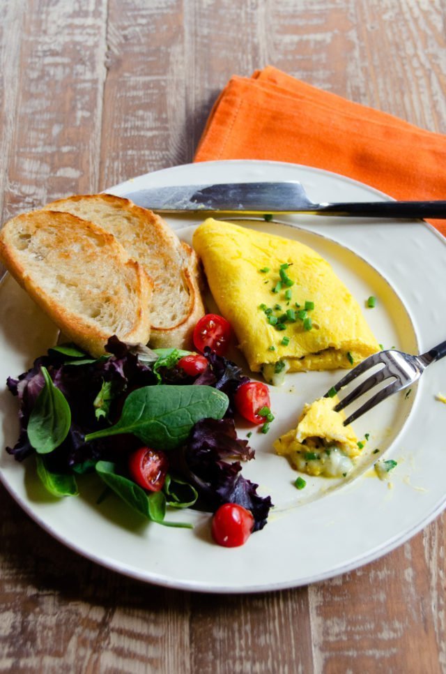 An omelet on a white plate with toasted bread and mixed greens.
