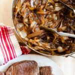 Browned beef on a plate and caramelized onions in a pan -ingredients for beef carbonnade.