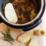 Layering mustard coated bread onto beef carbonnade in a pressure cooker.