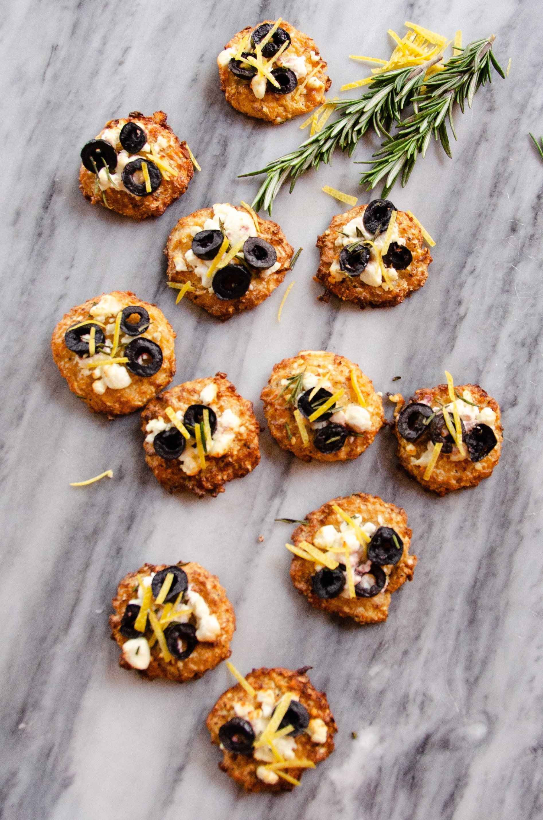 Goat cheese and olive cauliflower pizza bites on a marble counter.