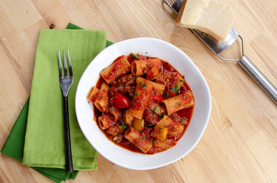 Rigatoni with Italian Sausage in a white bowl on a wooden table.