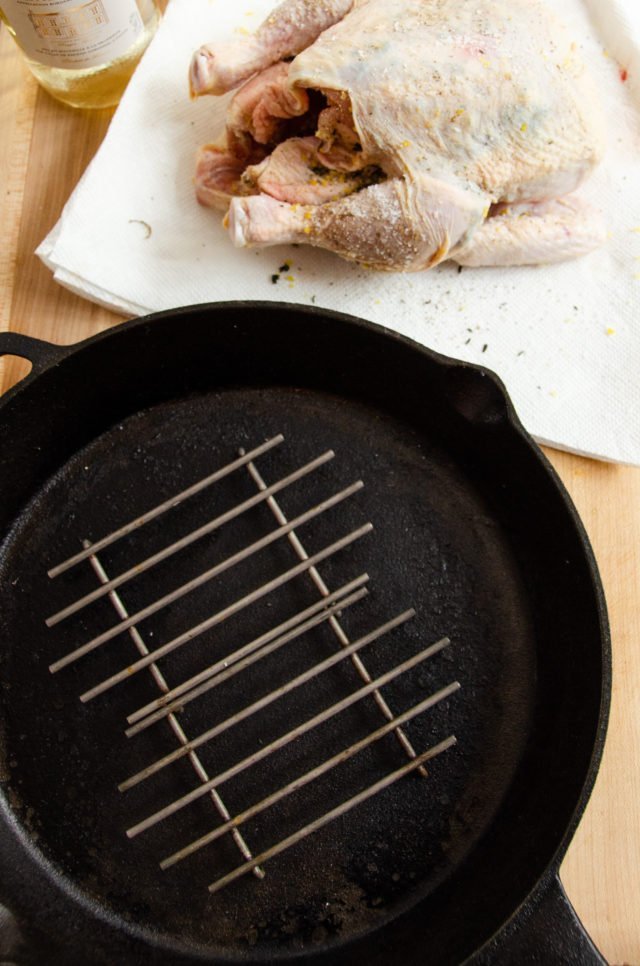 A seasoned raw roast chicken and a cast iron skillet with mini roasting racks inside.