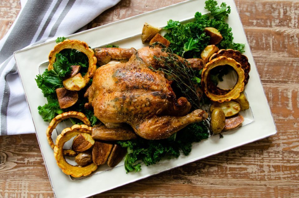Roast chicken with delicate squash, potatoes and kale on a white rectangular platter.