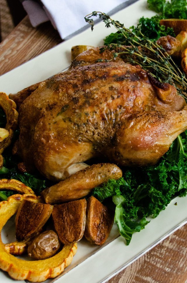 Roast chicken with delicate squash, potatoes and kale on a white rectangular platter.