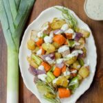 Root Vegetable Toss on a white oval plate with a leek beside it.