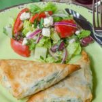 Spinach and Ricotta Phyllo Pockets on a green plate with a side of Greek Salad.