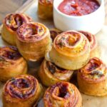 Air fried stromboli Pinwheels on parchment on a wooden board with a dish of marinara in the background.