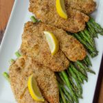 Lemon almond tilapia on a bed of asparagus on a white rectangular plate.