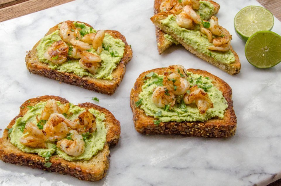 Four slices of edamame avocado toast on marble with a halved lime.