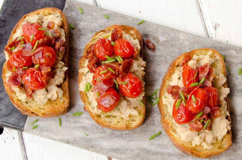 Overhead shot of three slices of White Bean Toast on a grey marble board.