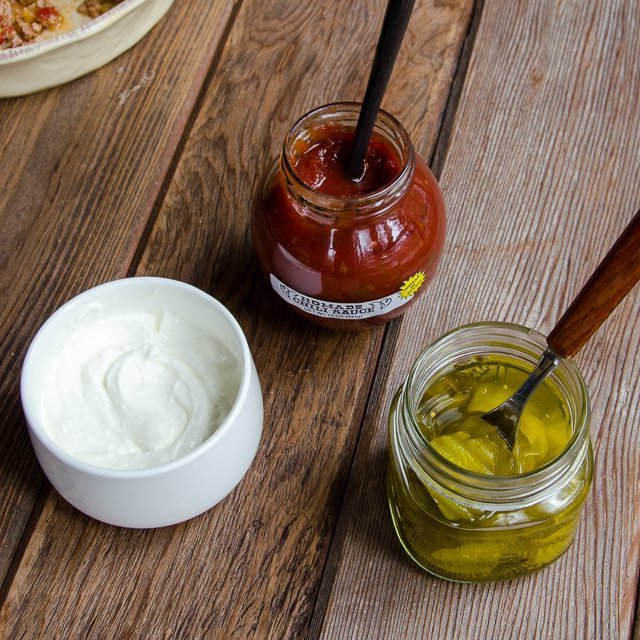 The condiments that accompany tourtière - sour cream, chili sauce and pickles in little jars on a wooden table.