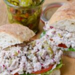 Tuna Salad Sandwich on ciabatta bread with bread and butter pickles in the background.
