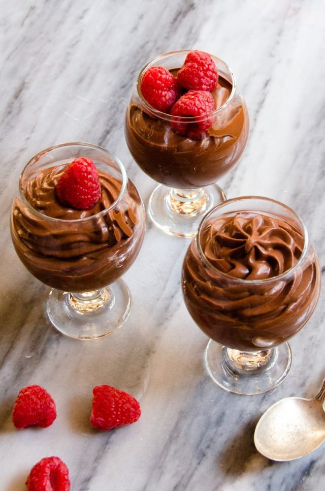 Three class dishes with Hervé This' Chocolate Mousse piped into them on a marble countertop.