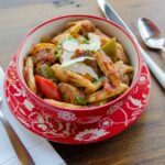Penne Pasta with sausage in a red bowl with place setting.
