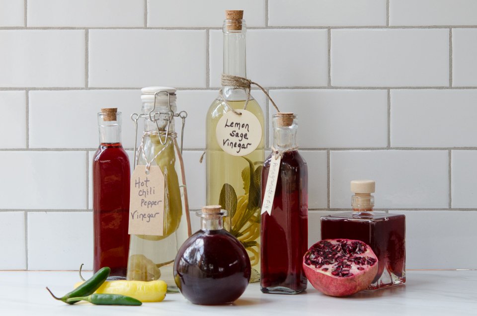 Homemade Flavored Vinegars on a counter with half a pomegranate and some hot peppers.