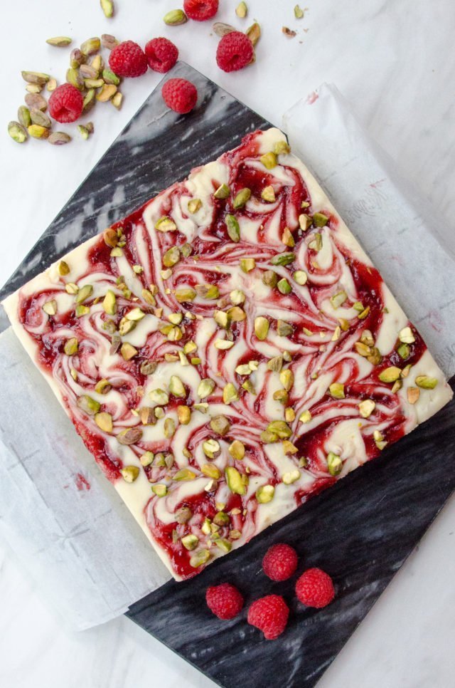 A large slab of white chocolate raspberry fudge with parchment paper on a black marble.
