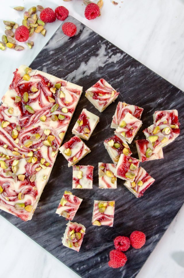 White chocolate raspberry fudge on black marble with some squares already cut.