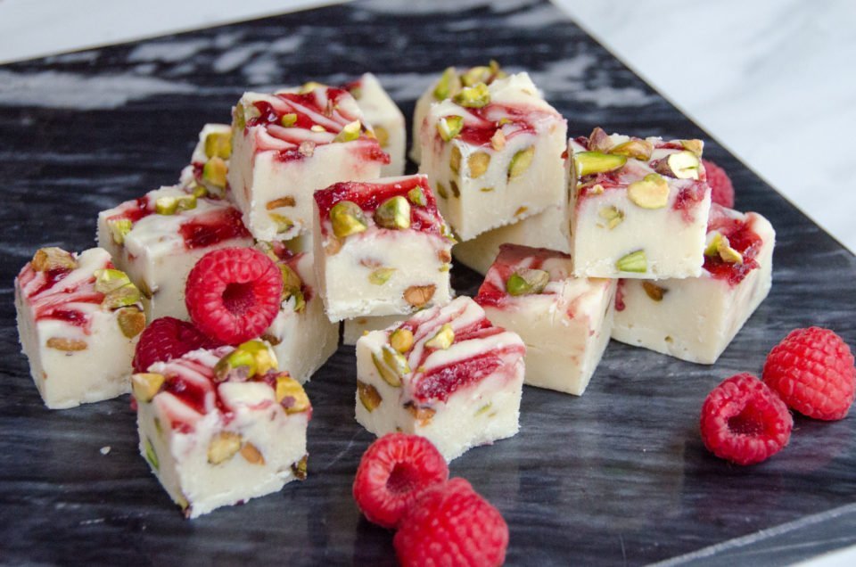 Squares of white chocolate raspberry fudge on black marble with fresh raspberries.