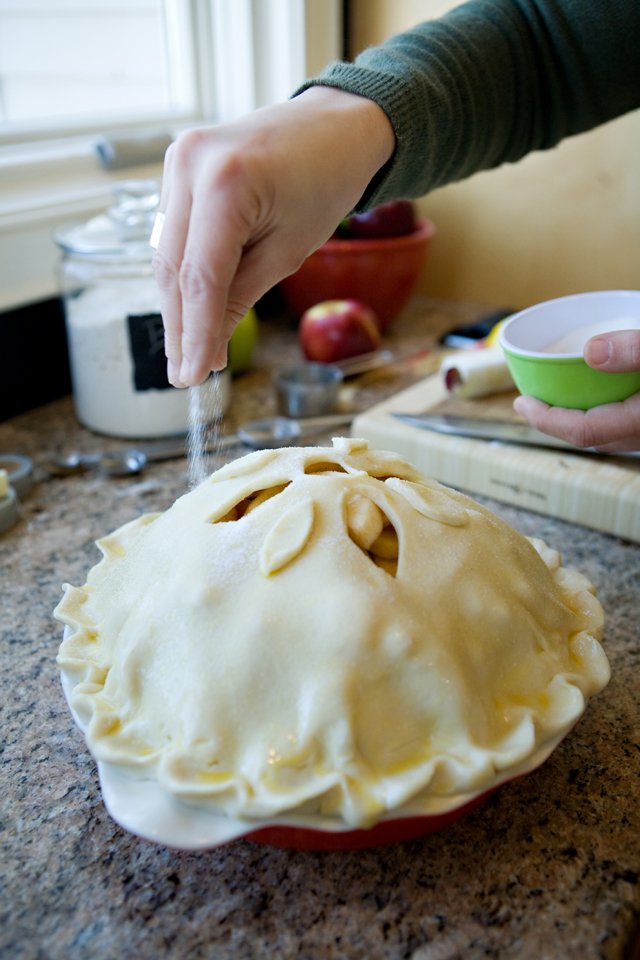 Sprinkling sugar on top of Mile High Apple Pie before baking.
