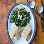 Black cod with grapes, kale and pecans on an oval white plate.