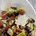 Brussels sprouts with bacon, parmesan cheese and balsamic reduction in a white bowl.