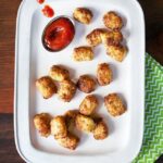 Cauliflower tater tots on a white plate with ketchup.