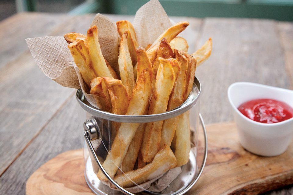 Homemade air-fried French fries in a clear bucket with ketchup on the side.