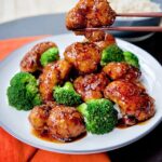 General Tso's Cauliflower on a white plate with chopsticks holding one piece up.