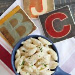 A blue crock with quick and easy mac and cheese in it on a red and white towel.