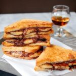 Midnight Nutella® banana sandwich on a grey platter with a glass of brandy in the background.