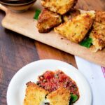 mozzarella en carrozza on a white plate with puttanesca sauce and more mozzarella en carrozza behind.