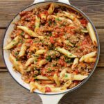 A white cast iron pot of One Pot Bolognese on a wooden table.