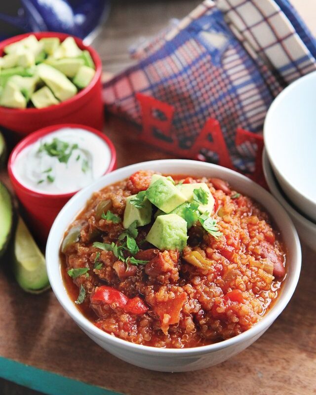 Quinoa chili in a white bowl with sour cream and avocado in dishes near by.