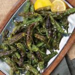 Shishito peppers on a silver tray with lemon.