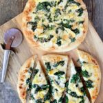 Spinach and Artichoke white pizza on a cutting board with a pizza wheel.