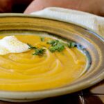 curried sweet potato soup in a bowl with some sweet potatoes in the background.
