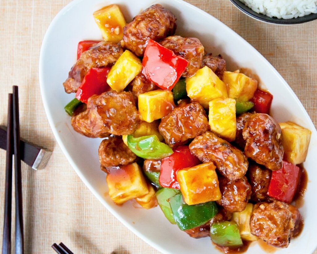 Sweet and sour pork on a white plate on a peach placement.