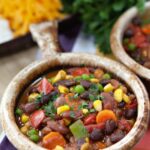 three bean vegetarian chili in a crock on a striped placemat.
