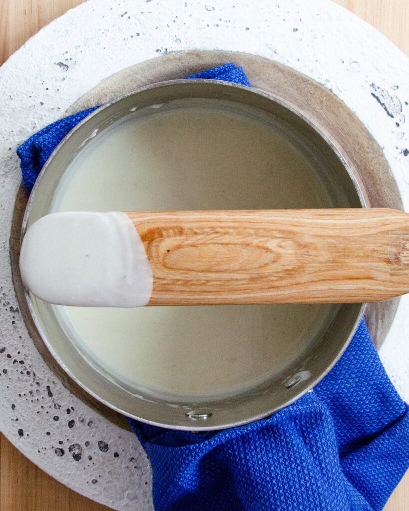 A wooden spoon over a pot of Béchamel sauce.